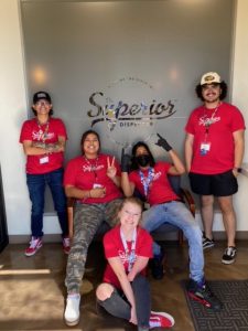 a group of young adults wearing red superior shirt posing in front of building.